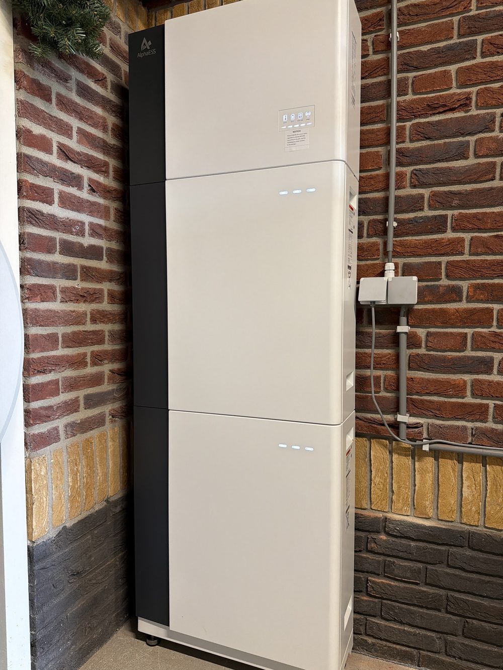 Een Alpha ESS-thuisbatterij binnen tegen een rode bakstenen muur