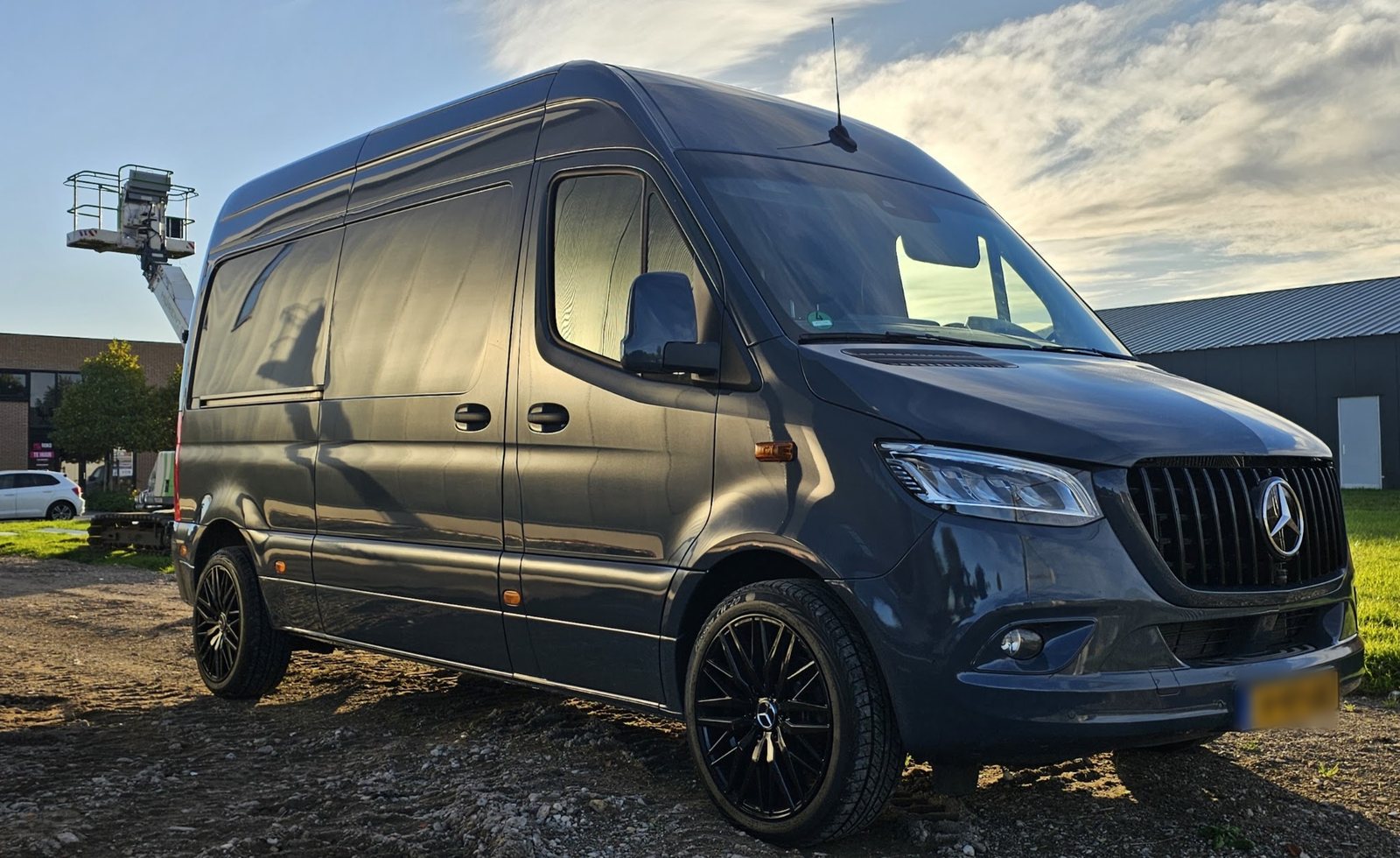 De donkergrijze Mercedes-bus van Multidiensten KEK op een grindterrein in het avondlicht