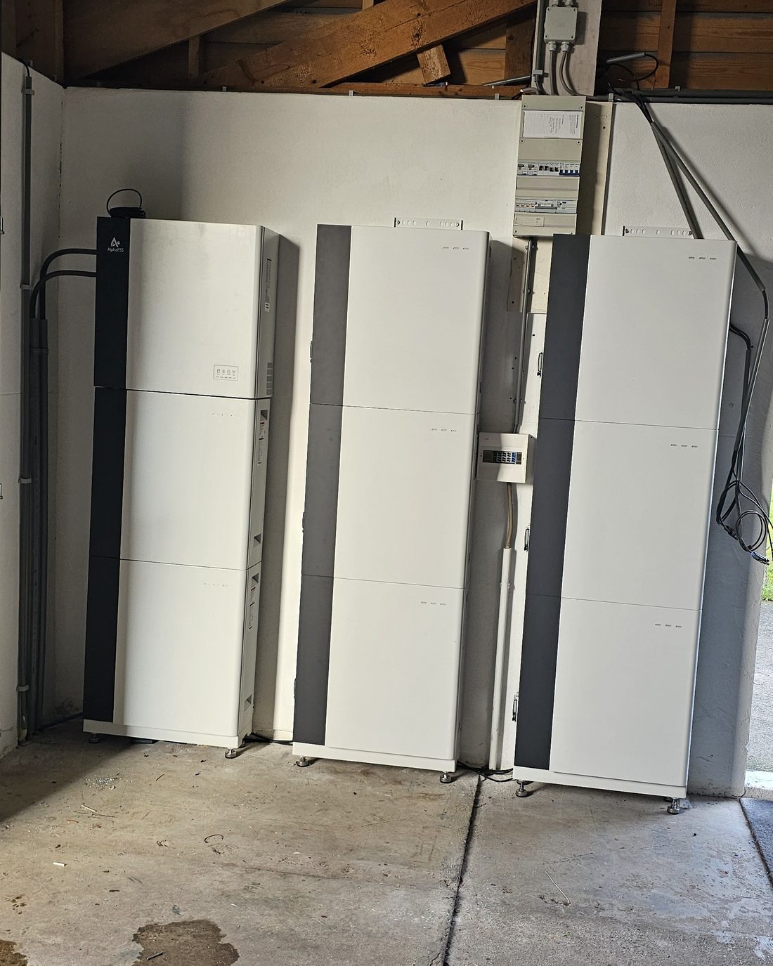 Drie Alpha ESS-thuisbatterijen naast elkaar in een garage, met de verdeelkast erboven