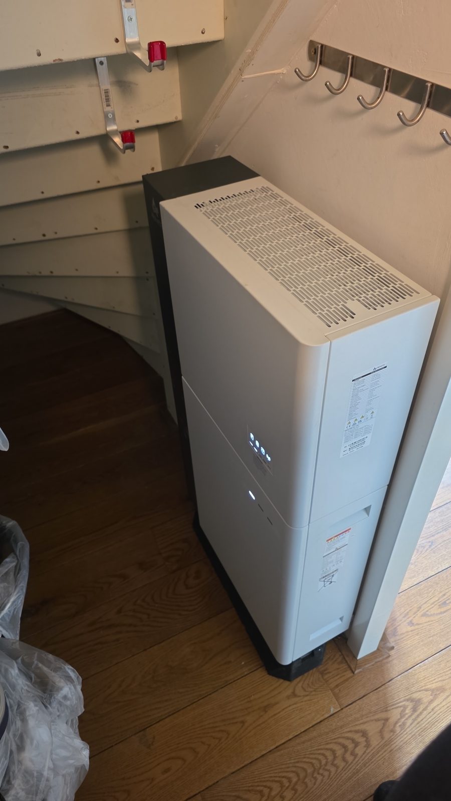 Een witte thuisbatterij precies passend onder een trap, naast een kapstok